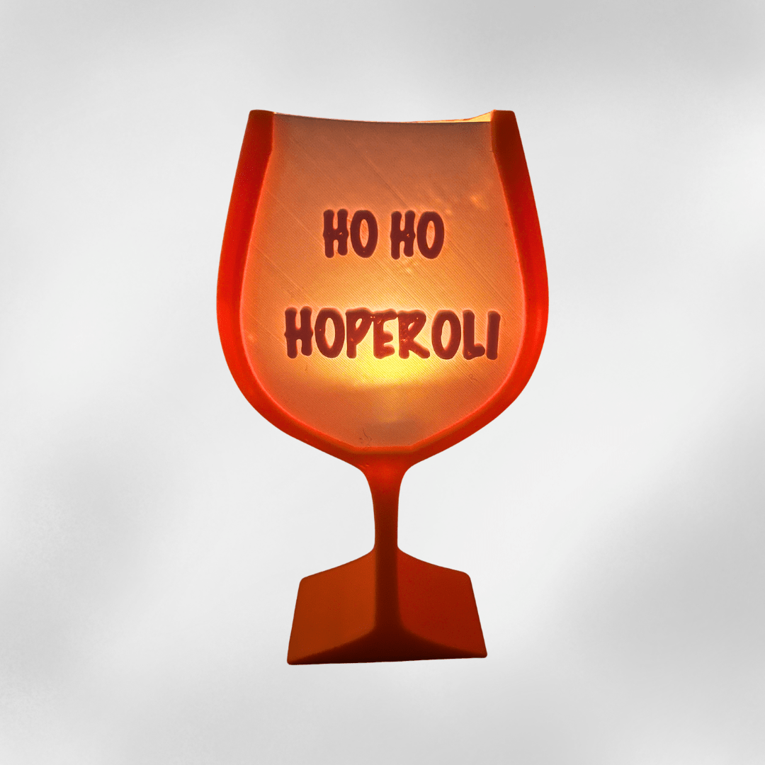 3D-gedruckte Weihnachtsdeko in Aperol-Optik, orangefarbenes Glas mit Schriftzug „Ho Ho Hoperoli“, leuchtend und festlich.