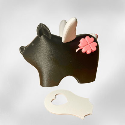 Schwarzes Sparschwein „Mathilde“ mit weißen Flügeln als liebevolle Kinderzimmer-Deko, platziert auf einem Holzregal mit warmem Licht – 3D-Druck aus dem Zauberwerk Onlineshop in Mittelhessen.